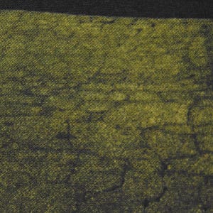 May include: Close-up of textured fabric in olive green with darker, irregular patterns, giving a distressed appearance. The fabric has a mottled effect. A black border is at the top.