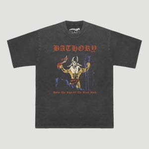 Op de afbeelding: Donkergrijs t-shirt met het woord "BATHORY" in rode gotische letters boven een afbeelding van een gehoornde figuur. De tekst "Under The Sign Of The Black Mark" staat eronder. Het shirt heeft een vintage, versleten uitstraling.