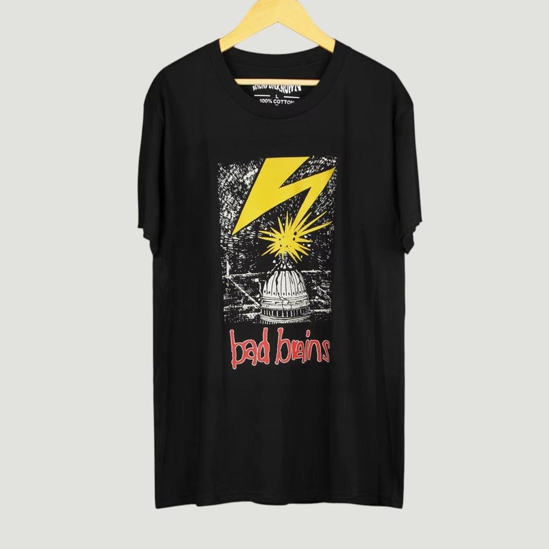 May include: A black short-sleeve t-shirt featuring a graphic print of a yellow lightning bolt striking a white building dome. Below the dome, the text "bad brains" is printed in red. The shirt has a crew neckline and is made of 100% cotton.