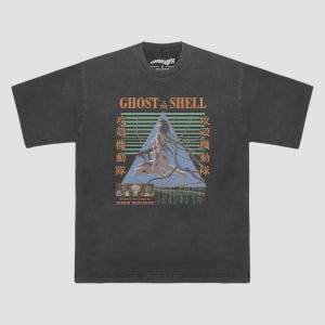 Può includere: T-shirt grigio scuro con la scritta "GHOST in the SHELL", caratteri giapponesi e una grafica di una figura all'interno di un triangolo. Il design è basato sul manga di Shirow Masamune.