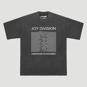 Op de afbeelding: Donkergrijs t-shirt met de tekst "JOY DIVISION" boven een witte golfvormige afbeelding en "UNKNOWN PLEASURES" eronder. Het shirt is gemaakt van een zacht materiaal en heeft een klassieke ronde hals.