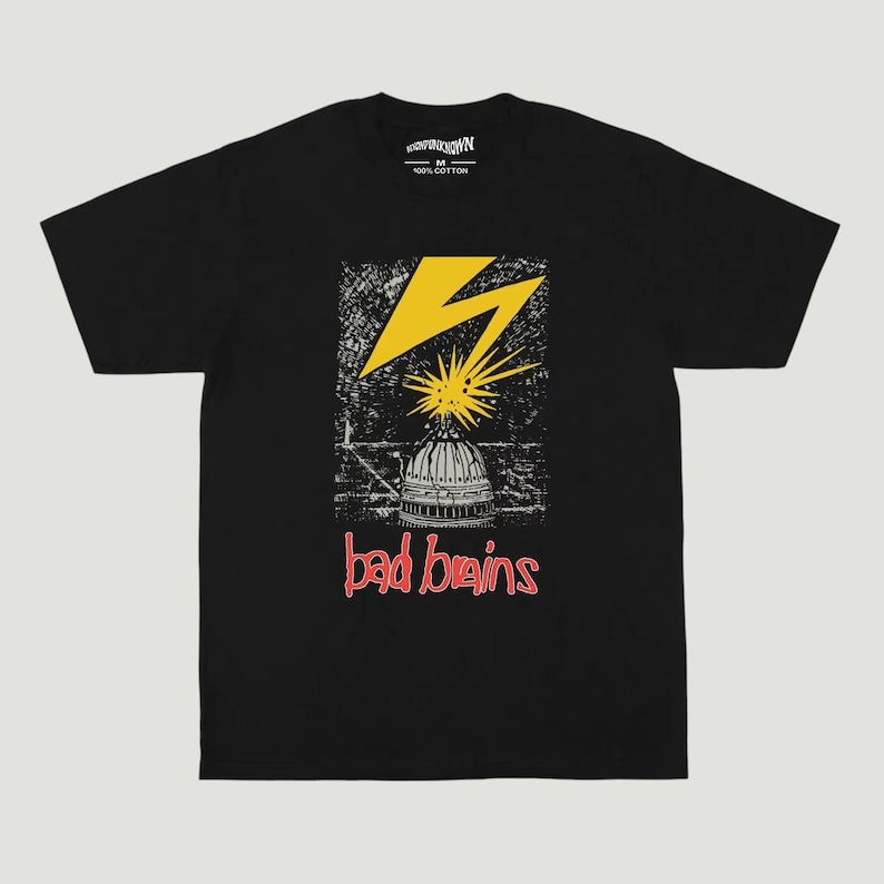 May include: A black short-sleeve t-shirt featuring a graphic print of a yellow lightning bolt striking a white dome building. Below the graphic, the text "bad brains" is printed in red. The interior neck label displays "HIGH PUNK NOWN" and "M 100% COTTON".