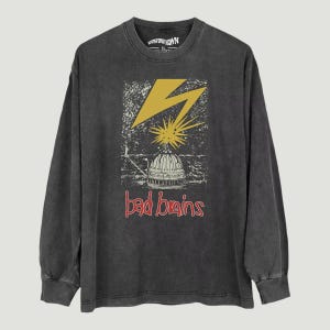 May include: A charcoal gray long-sleeve t-shirt featuring a graphic print of a yellow lightning bolt striking a building dome. The text "bad brains" is printed in red below the dome, and the inner neck label reads "BEYOND PUNKOWN XL".