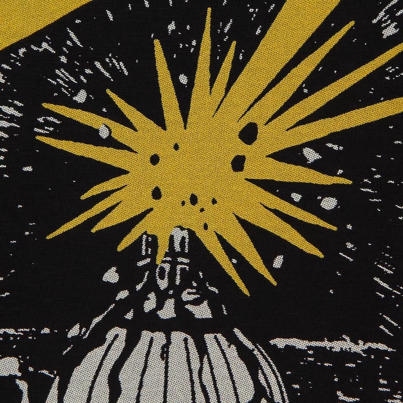 May include: A black fabric featuring a graphic print of a large, yellow, multi-pointed starburst shape positioned above a white, dome-like structure. The design includes scattered white dots against the black background, creating a celestial effect.
