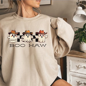 May include: A beige sweatshirt with a graphic of three cartoon ghosts wearing cowboy hats and the text "BOO HAW" printed on the front.