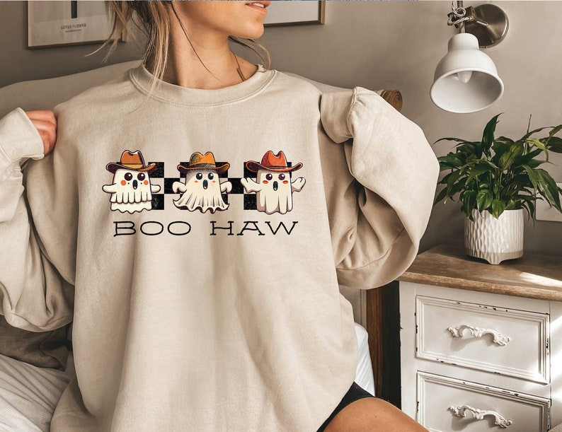 May include: A beige sweatshirt with a graphic of three cartoon ghosts wearing cowboy hats and the text "BOO HAW" printed on the front.