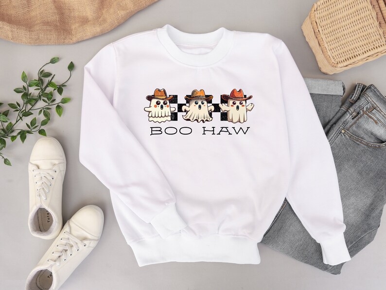 May include: White sweatshirt featuring a design of three ghosts wearing cowboy hats and the text "BOO HAW" on a black and white chequered background.