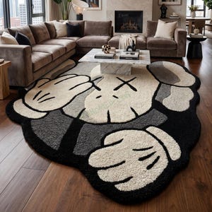 May include: A large, plush rug with a cartoon character design in a living room setting. The rug features a white, black, and gray color scheme, with a distinctive character face and hand motif. The rug is placed on a hardwood floor.