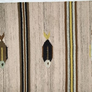 May include: A rectangular beige rug with vertical stripes and fish-like motifs. The rug features brown, yellow, and black stripes, with the fish designs in varying colors. The rug is made of woven material and is suitable for home decor.