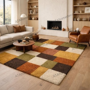 Könnte beinhalten: Ein großer, rechteckiger Teppich mit einem geometrischen Muster aus Quadraten in Creme, Braun, Orange, Gelb und Grün. Der Teppich liegt auf einem Holzboden in einem Wohnzimmer, mit einem Sofa und einem Sessel. Das Design des Teppichs verleiht Wärme.