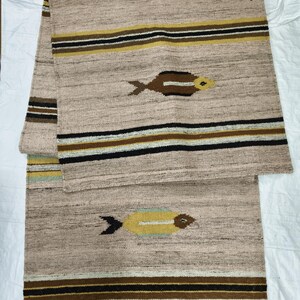 May include: Beige woven runner rug with a geometric pattern. The rug features horizontal stripes in black, brown, and yellow, and stylized fish motifs. The rug is made of a textured material and is suitable for a hallway or entryway.