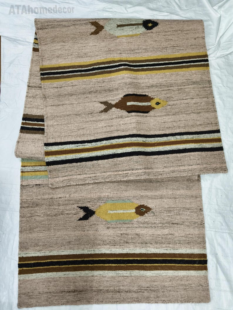 May include: Beige woven runner rug with a geometric pattern. The rug features horizontal stripes in black, brown, and yellow, and stylized fish motifs. The rug is made of a textured material and is suitable for a hallway or entryway.