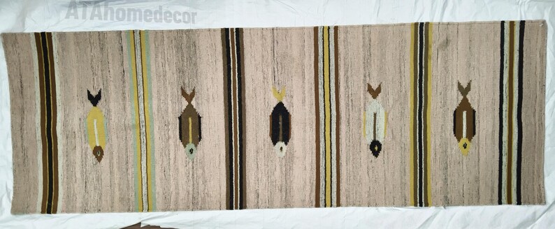 May include: A rectangular beige rug with vertical stripes and fish-like motifs. The rug features brown, yellow, and black stripes, with the fish designs in varying colors. The rug is made of woven material and is suitable for home decor.