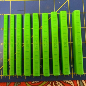 May include: A set of ten green plastic measuring sticks, each with a different length, ranging from 6 to 15 inches. The sticks are marked with numbers and lines to indicate the measurements.