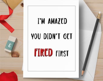 Könnte beinhalten: Eine weiße Grußkarte mit dem Text "I'M AMAZED YOU DIDN'T GET FIRED FIRST" in einem schwarzen Rahmen. Das Wort "FIRED" ist rot. Ein Bleistift, ein Umschlag, ein Radiergummi und ein rotes Band sind ebenfalls zu sehen.