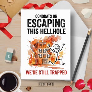 May include: A white greeting card with the text "CONGRATS ON ESCAPING THIS HELLHOLE" and "WE'RE STILL TRAPPED". The card features a cartoon illustration of a burning building and a stick figure running away. The card is on a wooden surface.