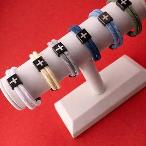 May include: A white ceramic mug with a black handle and the text "But First, Coffee" in a handwritten style. The mug is on a white surface. The mug is approximately 10 cm tall.