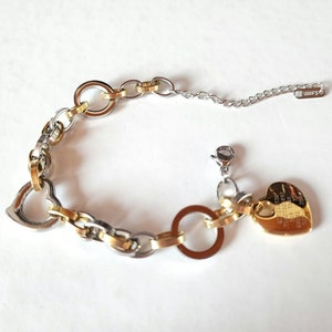 May include: A gold and silver bracelet with a heart charm. The charm has an inscription on it. The bracelet has a lobster clasp.