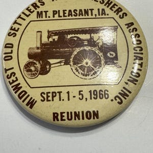 Può includere: Un bottone marrone e bianco con il testo "Midwest Old Settlers and Threshers Association, Inc." e "Mt. Pleasant, IA." Il bottone ha anche il testo "Sept. 1-5, 1966 Reunion" e un'immagine di una macchina a vapore.