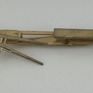 May include: A gold-toned multi-tool compass with a ruler and protractor. The tool is closed and has a 'C.C.' marking on the side.