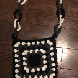 May include: A black, white, and gray crocheted bag with a chain strap. The bag is made of granny squares.