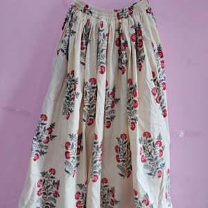 Puede incluir: Una falda de color crema con estampado floral en tonos rojos y grises. La falda tiene una cintura elástica y una silueta fluida.