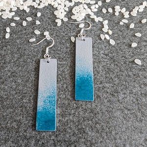 May include: A pair of silver dangle earrings with a rectangular blue and gray design. The earrings have a gradient effect, fading from a light gray to a dark blue.