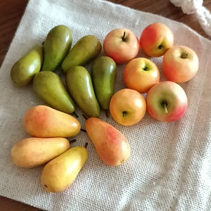 Op de afbeelding: Een verzameling groene peren en gele en rode appels gerangschikt op een wit stofoppervlak.