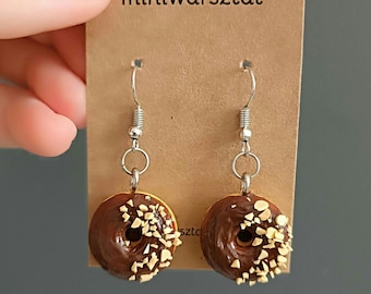 May include: A pair of dangle earrings featuring a chocolate glazed donut with sprinkles. The donuts are made of polymer clay and are attached to silver-toned hooks.