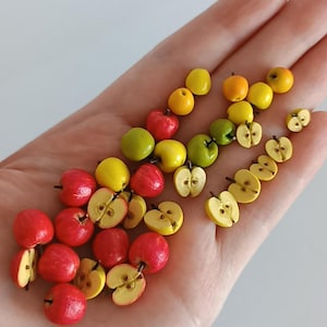 Puede incluir: Una colección de manzanas rojas, amarillas y verdes en miniatura, algunas enteras y otras cortadas por la mitad. Las manzanas están dispuestas en un degradado de verde a amarillo a rojo.