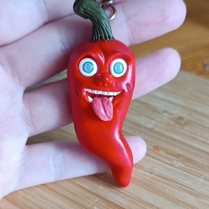 May include: A red chilli pepper keychain with a cartoon face, blue eyes, and a pink tongue sticking out.
