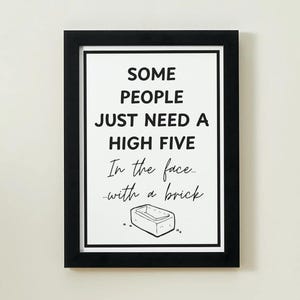 May include: A framed print with a white background and black text that reads "SOME PEOPLE JUST NEED A HIGH FIVE In the face... with a brick." A small brick illustration is at the bottom. The frame is black.