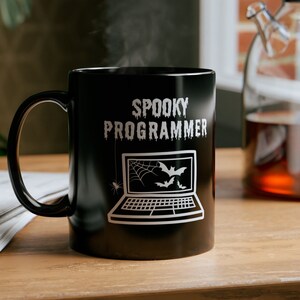 Peut inclure: Mug à café noir avec un motif blanc d'un ordinateur portable avec des chauves-souris et une toile d'araignée. Le texte "Spooky Programmer" est imprimé sur la tasse.