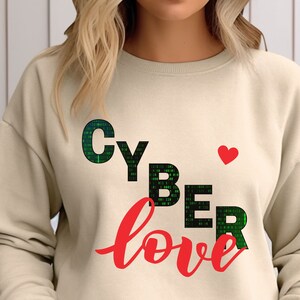 May include: A beige sweatshirt with the text "CYBER love" in green and red. The word "CYBER" is made up of green code and the word "love" is in red cursive. A small red heart is above the word "love".