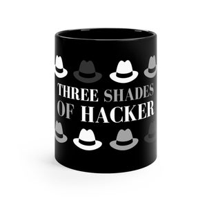 Puede incluir: Taza de café negra con texto blanco que dice "Three Shades of Hacker" y un patrón de sombreros fedora blancos, grises y negros.