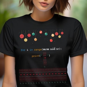 May include: Black t-shirt with a Christmas-themed design featuring a line of colorful ornaments and the code "for i in range(mom said so): print('')".