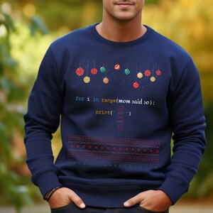 K&ouml;nnte beinhalten: Ein marineblauer Pullover mit einem Weihnachtsbaum-Design aus bunten Kugeln. Der Pullover hat eine Zeile Code darauf gedruckt, die lautet: "for i in range(mom said so): print('')".
