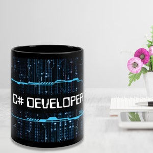 Könnte beinhalten: Schwarze Keramik-Kaffeetasse mit einem blauen und schwarzen digitalen Muster und dem Text "C# DEVELOPER" auf der Vorderseite.