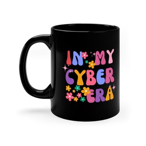 Peut inclure: Mug en céramique noire avec un motif blanc qui dit "In My Cyber Era" en lettres colorées de style rétro avec des fleurs et des paillettes.