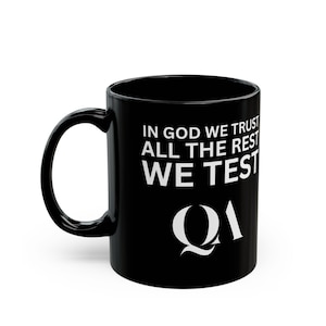 Può includere: Tazza da caffè in ceramica nera con testo bianco che recita "In God We Trust All The Rest We Test" e un logo "QA" bianco.
