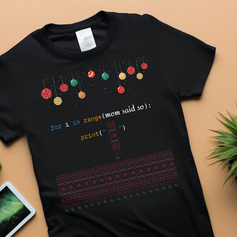 以下が含まれることがあります： カラフルなオーナメントでできたクリスマスツリーのデザインと、「for i in range(mom said so): print('"')」というコード行が書かれた黒いTシャツ。