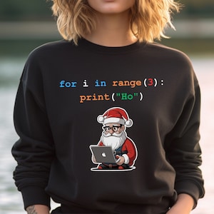 Può includere: Una felpa nera con un frammento di codice bianco, arancione e blu che recita "for i in range(3): print("Ho")". Un'immagine di cartone animato di Babbo Natale con occhiali e un cappello rosso che tiene un laptop con un logo Apple.