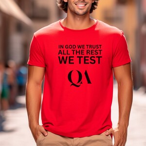 May include: Red t-shirt with the text "In God We Trust All The Rest We Test" and the letters "QA" in a stylized font.