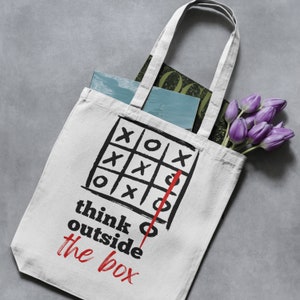 May include: White canvas tote bag with black and red graphic of a tic-tac-toe board with a red line drawn outside the box. The text "think outside the box" is written below the graphic.