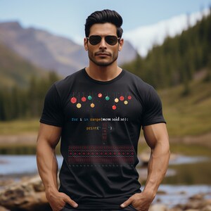 以下が含まれることがあります： カラフルなオーナメントと「for i in range(mom said so): print('')」というコードでできたクリスマスツリーのデザインが施された黒いTシャツ。