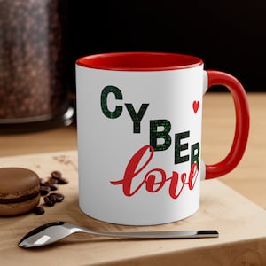 Puede incluir: Taza de cerámica blanca con borde y asa rojos. La taza tiene el texto "CYBER love" impreso en negro y rojo. La palabra "CYBER" está formada por código binario verde.