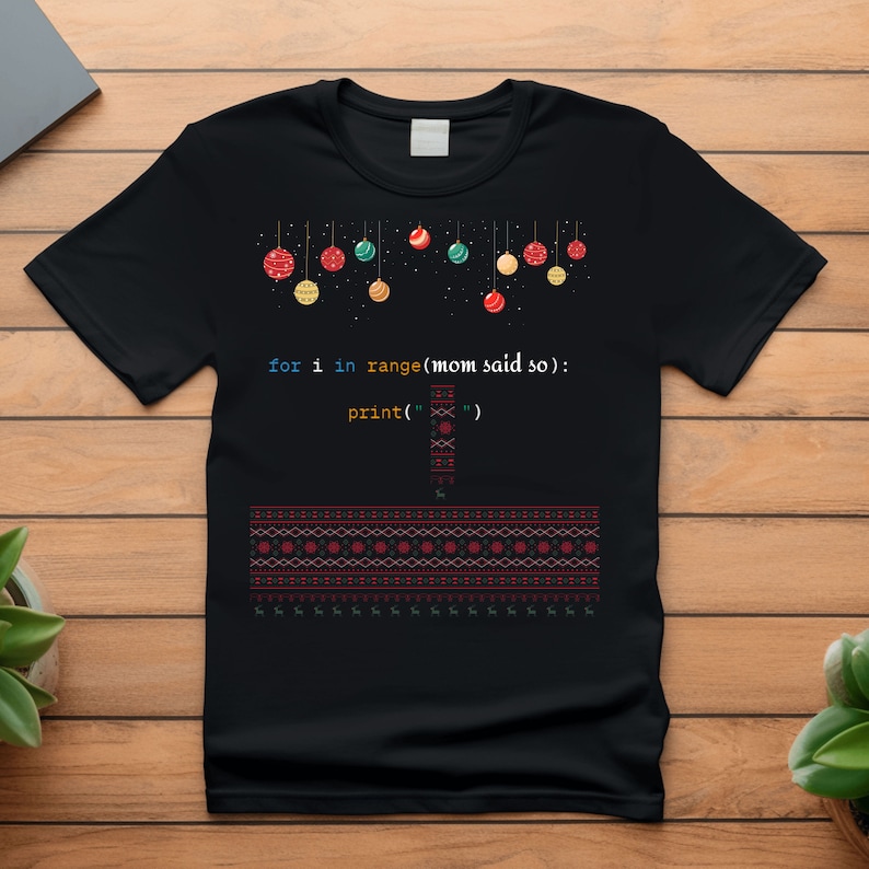 以下が含まれることがあります： カラフルなオーナメントでできたクリスマスツリーのデザインと、「for i in range(mom said so): print('')」というコード行が書かれた黒いTシャツ。