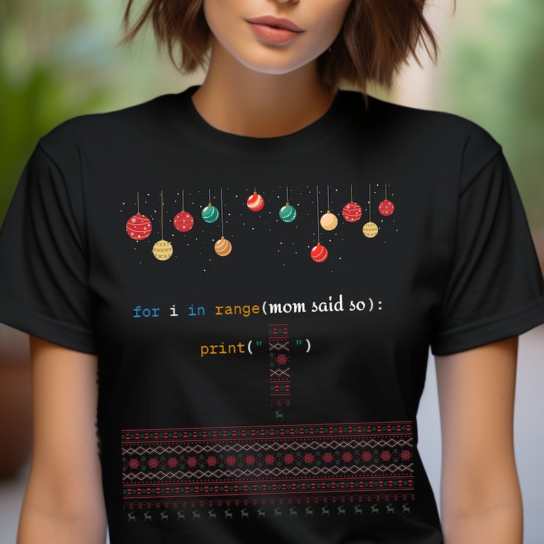 以下が含まれることがあります： クリスマスをテーマにしたデザインの黒いTシャツ。カラフルなオーナメントの列とコード「for i in range(mom said so): print('')」が描かれています。
