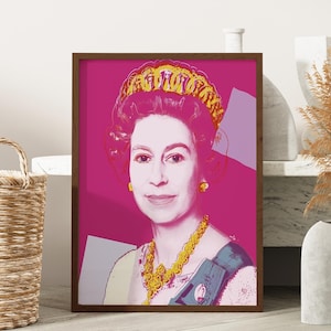 May include: A framed pop art style portrait of a woman with a magenta background. The portrait features a woman with a gold crown, earrings, and necklace. The artwork is in a dark brown frame and is displayed on a light-colored surface.