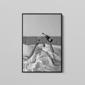 以下が含まれることがあります： ベッドでシャンパンのグラスとボトルを持っている人の白黒写真です